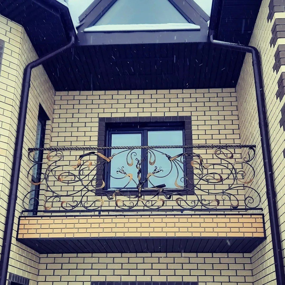 Кованое балконное ограждение с золочёными завитками на фасаде из жёлтого кирпича